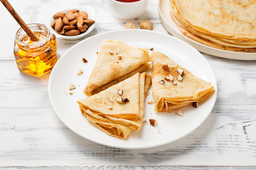 Crepes, thin pancakes with honey and nuts on a white plate . Wooden background .