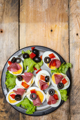 a plate of hard-boiled eggs, with the addition of mayonnaise, green leaves of lettuce, black olives and pieces of salami