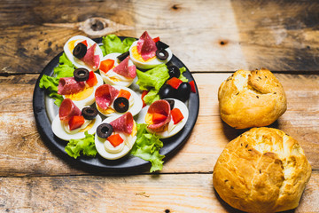 a plate of hard-boiled eggs, with the addition of mayonnaise, green leaves of lettuce, black olives and pieces of salami
