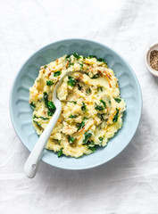 Mashed potatoes with spinach and crispy fried onions on a light background, top view. Delicious side dish or vegetarian meal