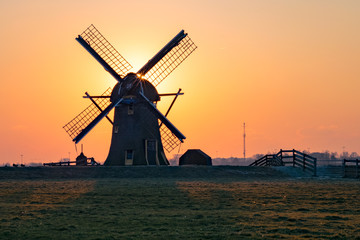 A classic dutch windmill, close to the city of Leiden, The Netherlands, stands clearly against the orange colored sky. Wide open dutch landscape at the end of a very cold day, end of February 2018.