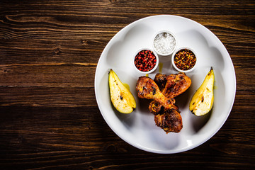 Grilled chicken drumsticks with pear on wooden background