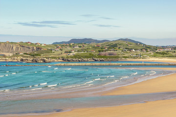 Beautiful Mediterranean seacoast, Cantabria, Spain. Bay, seaside, white foam and teal sea ocean water with small town and walking people