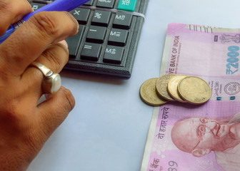Woman checking account with calculator and holding a pen with Indian currency notes coins....