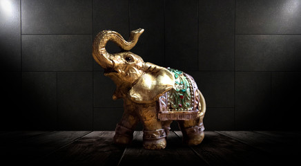 Golden elephant on a wooden table. Dark room, light effect. Beautiful statuette of an elephant on the background.