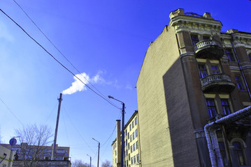 Old pipe with smoke, residential brick buildings corners with windows and wires on winter bright blue sky background, view from ground on top