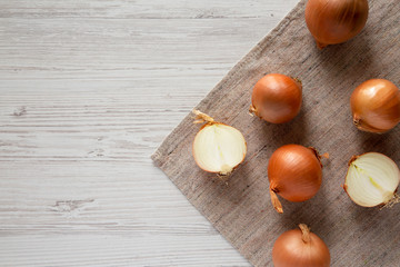 Overhead view, unpeeled raw yellow onions over white wooden surface, top view. Flat lay, flat lay, from above.
