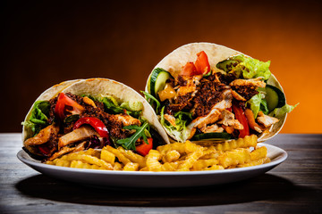 Kebab - grilled meat with french fries and vegetables on wooden background