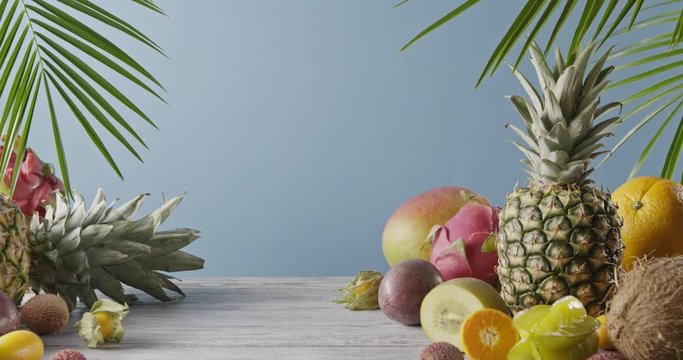 Various juicy exotic fruits - lychee, pineapple and carambola on a gray wooden table on a blue. Dolly out motion, 4K UHD video, 3840, 2160p.