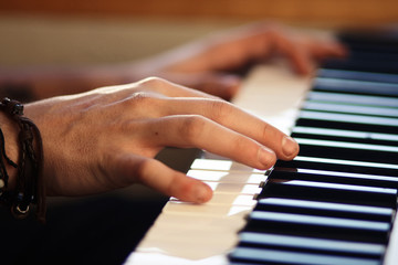 Fototapeta premium Hands, one of which is wearing a bracelet, playing a melody on a keyboard musical instrument