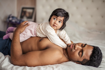 little baby lying on her sleeping daddy in the bedroom with modern interior, close up photo