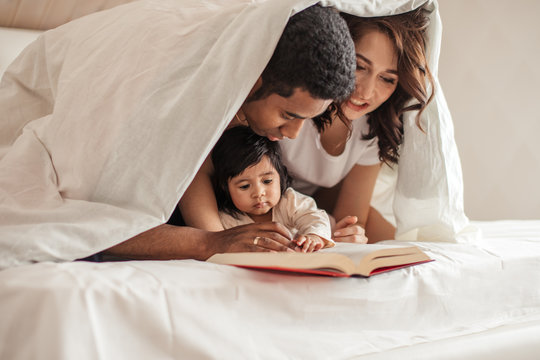 cute family turning over the pages in the book while sitting on the bed at home, close up photo