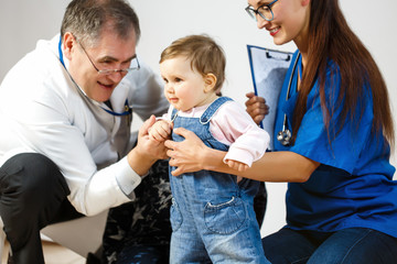 Two doctors examining a small child in a denim overalls