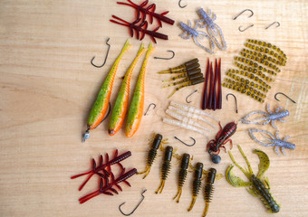 Fototapeta na wymiar Colorful silicone fishing baits with plummets on wooden table. Various fish and worms and crayfish. Toned image and top view. Stock background, photo