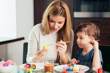Obraz na płótnie Canvas Young beautiful mother, being great with her adorable son, spend time together. Easter celebration and parenthood concept. Mother and son making Easter decorations at home.