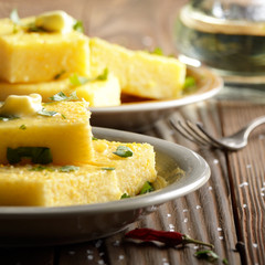 Polenta with butter and greens on clay dish on wooden rustic table