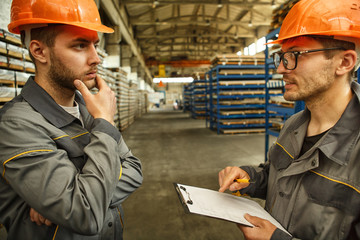 Two industrial workers checking stock with a clipboard