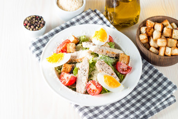 Fresh salad made of tomato, ruccola, chicken breast, eggs, arugula, crackers and spices. Caesar salad in a white, transparent bowl on wooden background