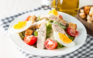 Fresh salad made of tomato, ruccola, chicken breast, eggs, arugula, crackers and spices. Caesar salad in a white, transparent bowl on wooden background