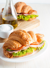 Fresh croissant or sandwich with salad, ham, jamon, prosciutto, salami, cheese, chicken, tomatoes on wooden background. Morning breakfast concept. Healthy and fast food.