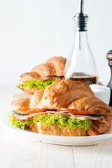 Fresh croissant or sandwich with salad, ham, jamon, prosciutto, salami, cheese, chicken, tomatoes on wooden background. Morning breakfast concept. Healthy and fast food.