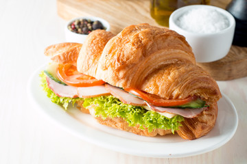 Fresh croissant or sandwich with salad, ham, jamon, prosciutto, salami, cheese, chicken, tomatoes on wooden background. Morning breakfast concept. Healthy and fast food.