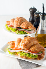 Fresh croissant or sandwich with salad, ham, jamon, prosciutto, salami, cheese, chicken, tomatoes on wooden background. Morning breakfast concept. Healthy and fast food.