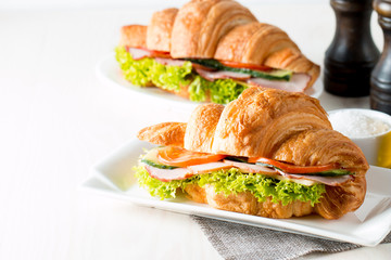 Fresh croissant or sandwich with salad, ham, jamon, prosciutto, salami, cheese, chicken, tomatoes on wooden background. Morning breakfast concept. Healthy and fast food.