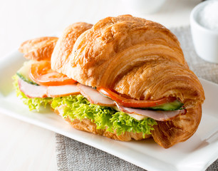 Fresh croissant or sandwich with salad, ham, jamon, prosciutto, salami, cheese, chicken, tomatoes on wooden background. Morning breakfast concept. Healthy and fast food.