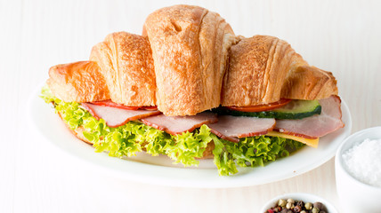 Fresh croissant or sandwich with salad, ham, jamon, prosciutto, salami, cheese, chicken, tomatoes on wooden background. Morning breakfast concept. Healthy and fast food.