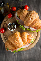 Fresh croissant or sandwich with salad, ham, jamon, prosciutto, salami, cheese, chicken, tomatoes on wooden background. Morning breakfast concept. Healthy and fast food.