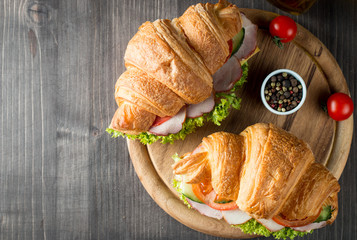 Fresh croissant or sandwich with salad, ham, jamon, prosciutto, salami, cheese, chicken, tomatoes on wooden background. Morning breakfast concept. Healthy and fast food.
