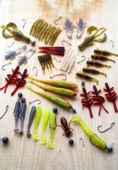 Obraz na płótnie Canvas Colorful silicone fishing baits with plummets on wooden table. Various fish and worms and crayfish. Toned image and top view. Stock background, photo