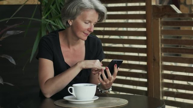 Handsome gray hair lady female using smartphone in cafe 4k