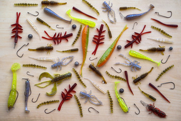 Obraz na płótnie Canvas Colorful silicone fishing baits with plummets on wooden table. Various fish and worms and crayfish. Toned image and top view. Stock background, photo