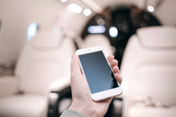 Man is holding mobile phone in business jet interior