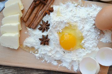 White flour with eggs, butter, cinnamon sticks, spicy anise stars and wooden spoon on a cooking board