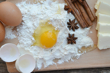 White flour with eggs, butter, cinnamon sticks, spicy anise stars and wooden spoon on a cooking board