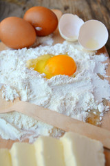 White flour with eggs, butter and wooden spoon on a cooking board