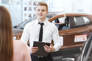 Young couple choosing a car with salesman at the dealership