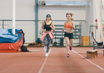 Fototapeta na wymiar Two young athletic women running in sports arena indoors