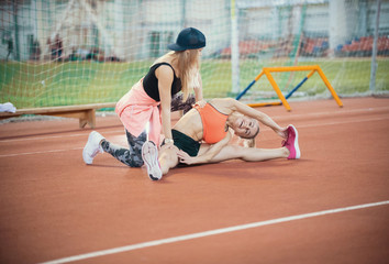 Two young beautiful women with blonde hair doing exercises and breathing hard in the sports hall