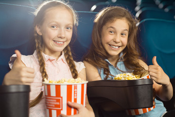 Cheerful young girl showing thumbs up at the cinema
