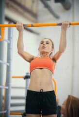 Naklejka premium Young woman with blonde hair pulls up on the crossbar in the sports hall
