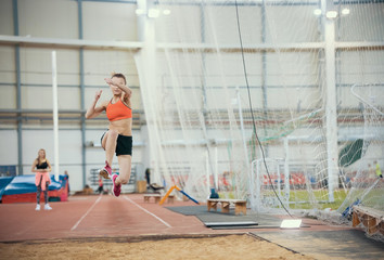 Young blonde women performing a long jump in the sports arena