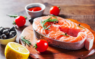 fresh raw salmon steak with tomato, lemon, olive, pepper, sauce and aromatic herbs on the wooden table background