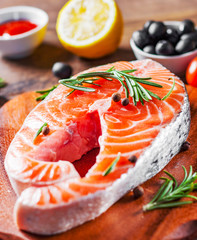 fresh raw salmon steak with tomato, lemon, olive, pepper, sauce and aromatic herbs on the wooden table background