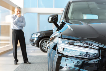 Mature man choosing a new car to buy at the dealership showroom