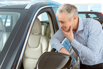 Mature man choosing a new car to buy at the dealership showroom