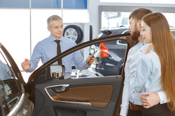 Obraz premium Professional car dealer showing a new car to young couple at the dealership center